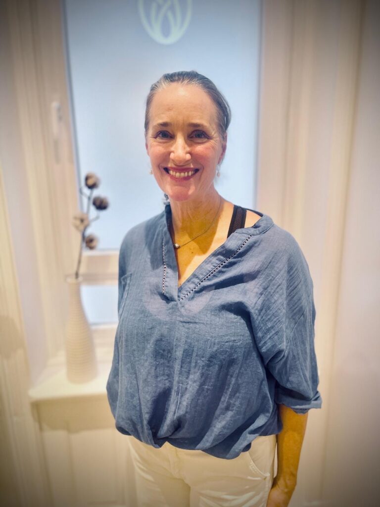 Portrait von Adrienne lächelnd vor Fenster in der Praxis